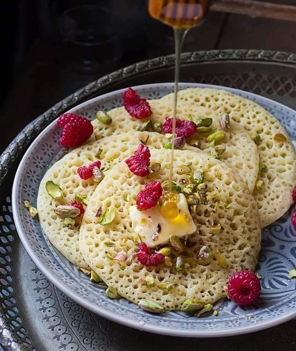 Baghrir con miel, frambuesas y mantequilla en un plato de cristal